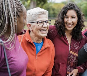 Group of three women, varying ages, smiling/laughing outdoors, dressed in casual clothes.