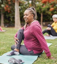 Middle-aged woman doing yoga on mat in park.