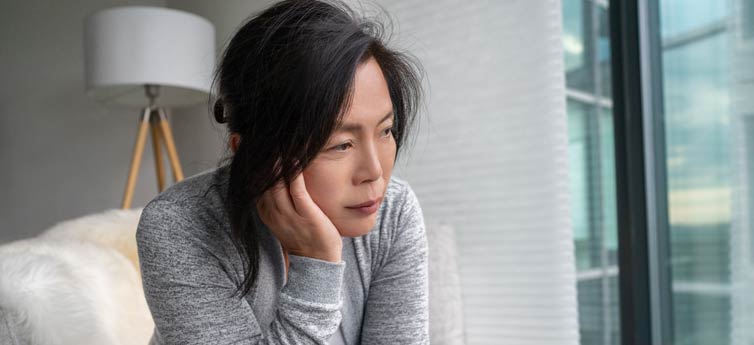 Woman, sitting in an upholstered chair and resting her face in her palm, stares blankly ahead.