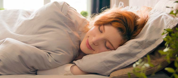 Woman contentedly sleeping with morning sunshine coming through a window behind her.