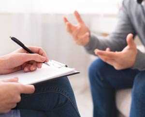 Patient’s hands gesturing with therapist writing notes on a clipboard.