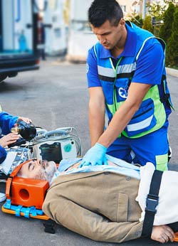 Emergency medical technicians performing CPR on a man on a stretcher wearing a neck brace.