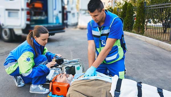 Emergency medical technicians performing CPR on a man on a stretcher wearing a neck brace.