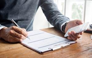 Person at desk completing a form on a clipboard.