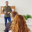 Younger man talking to a room of attendees in a classroom setting.