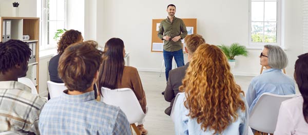 Younger man talking to a room of attendees in a classroom setting.