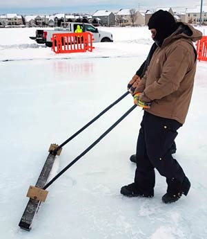 Worker using a snow broom to clear ground.