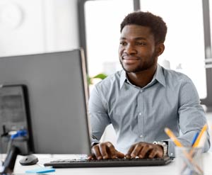 Young professional man smiling at computer monitor with hands on keyboard.